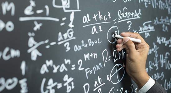 Hand writing mathematical equations on chalkboard.