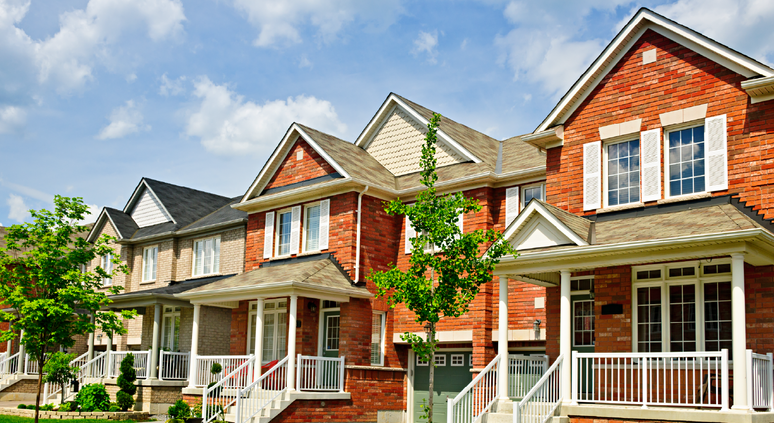 Row of brick townhouses with front porches under a blue sky.