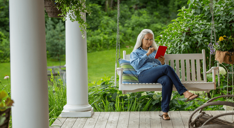 A woman reading a book on a porch swing surrounded by greenery.