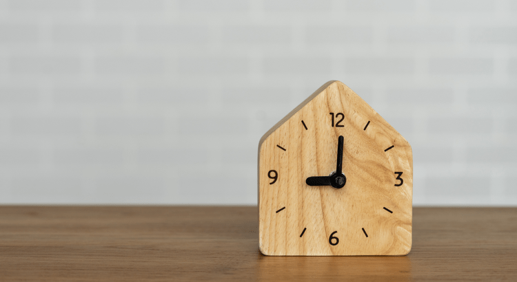 Wooden clock shaped like a house showing 3 o'clock.
