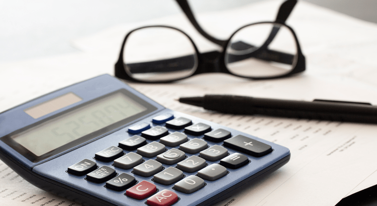 Calculator, pen, and glasses on a white desk.